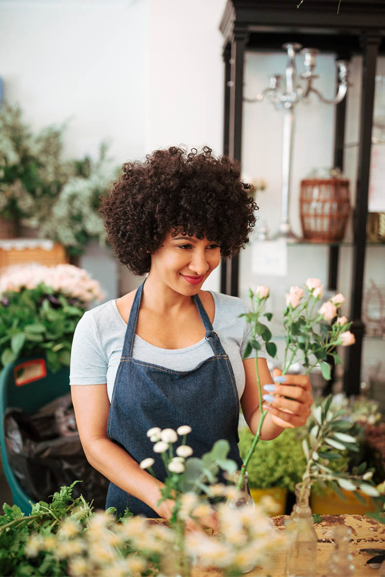 A florist business owner arranging-flowers in glass vase in her floral shop.