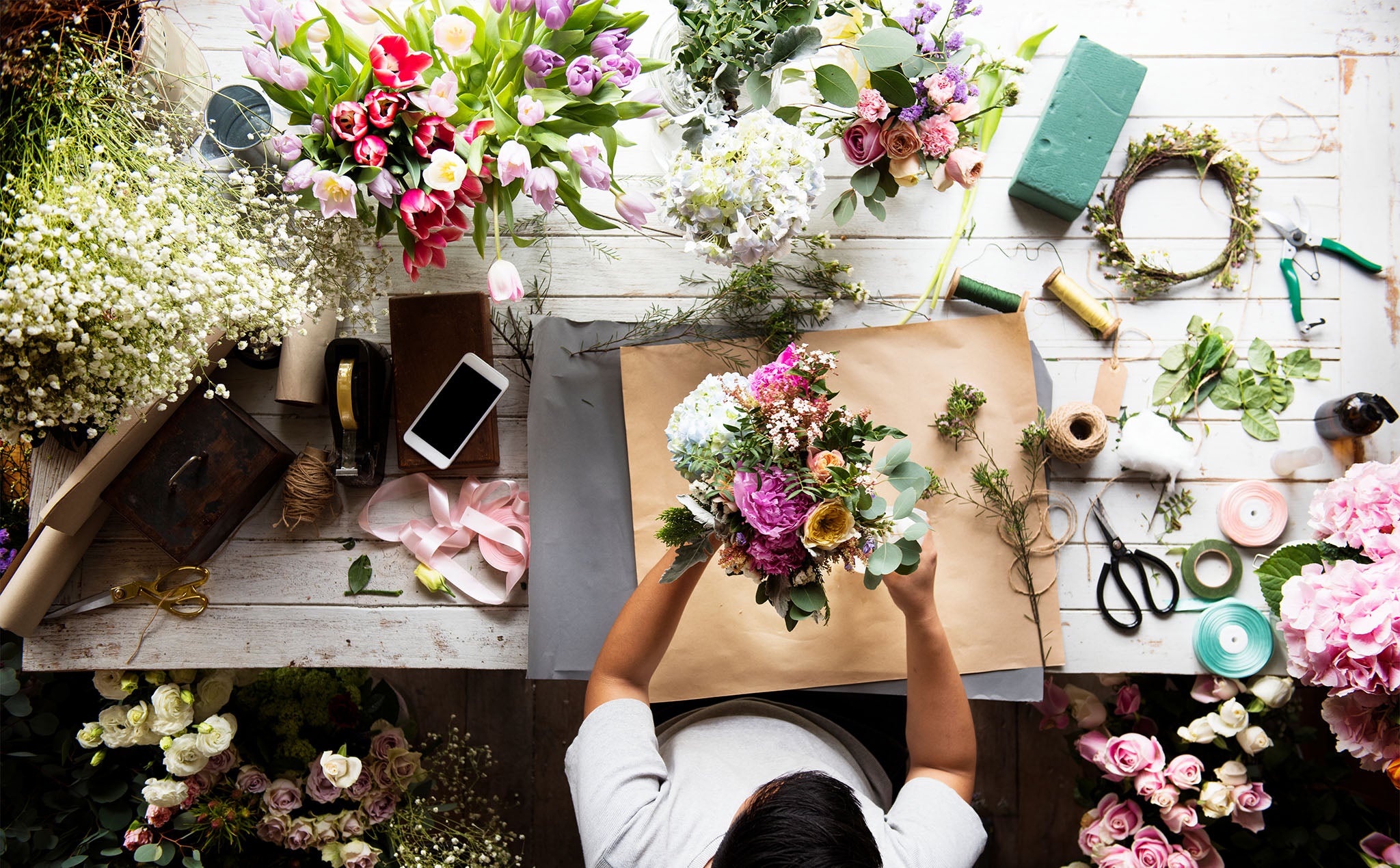 Florist at work with flowers and tools on a wooden table.