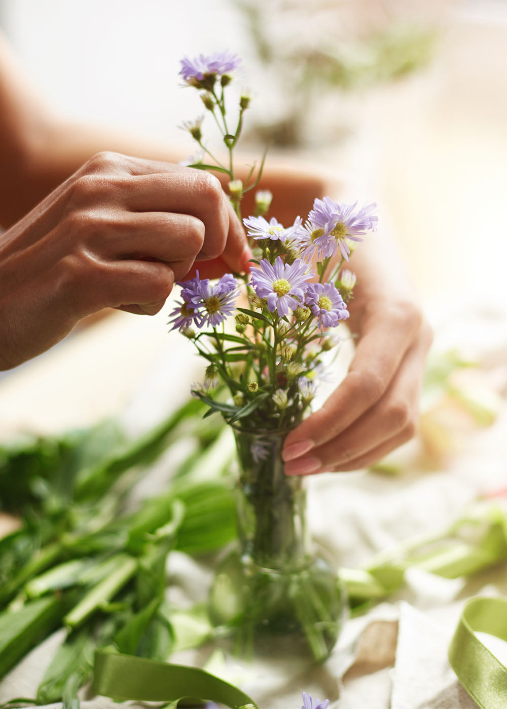 A florist arranging flowers in a vase in her flower shop with a blurred natural background.