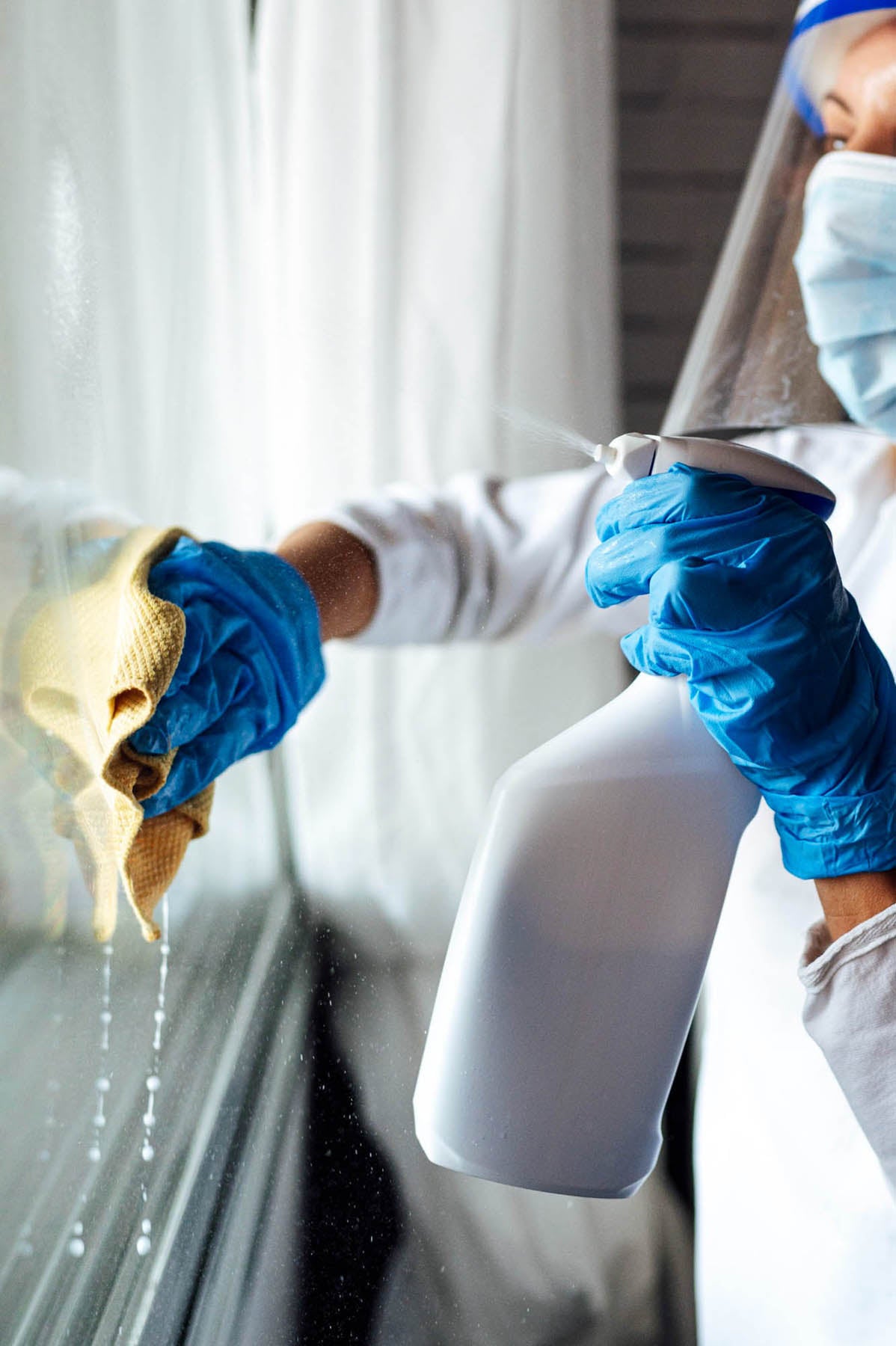 Cleaning staff disinfecting window whilst wearing ppe.