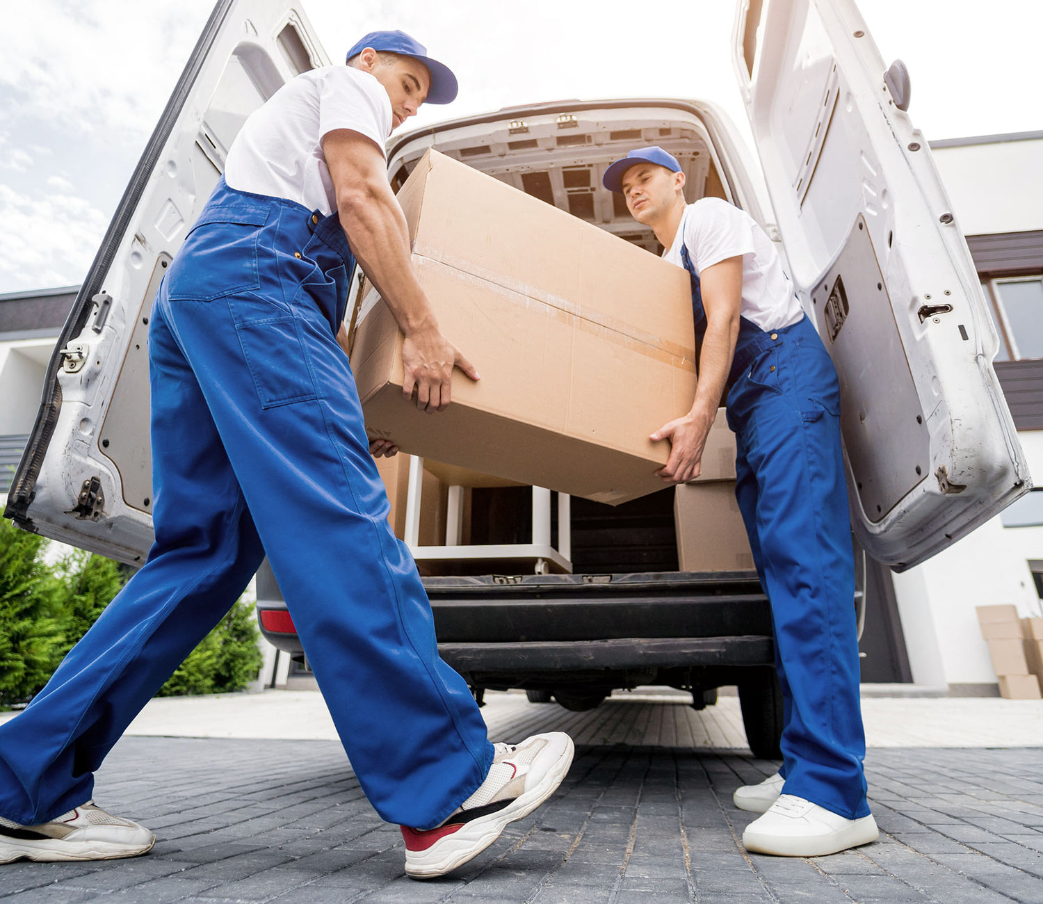 Two removal company workers unloading boxes of furniture from their van.