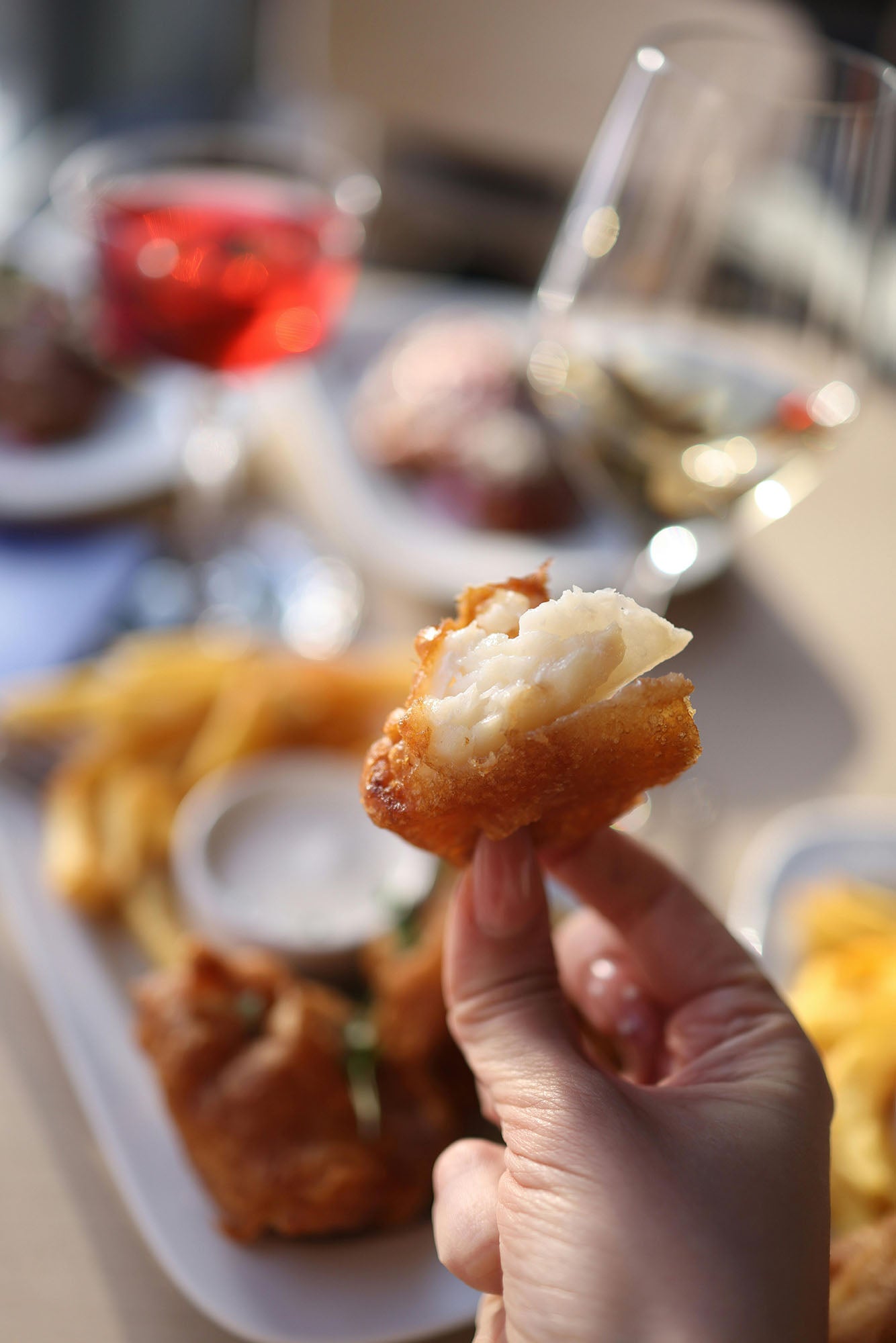A hand holding a piece-of battered fish in a fish and chip restaurant.