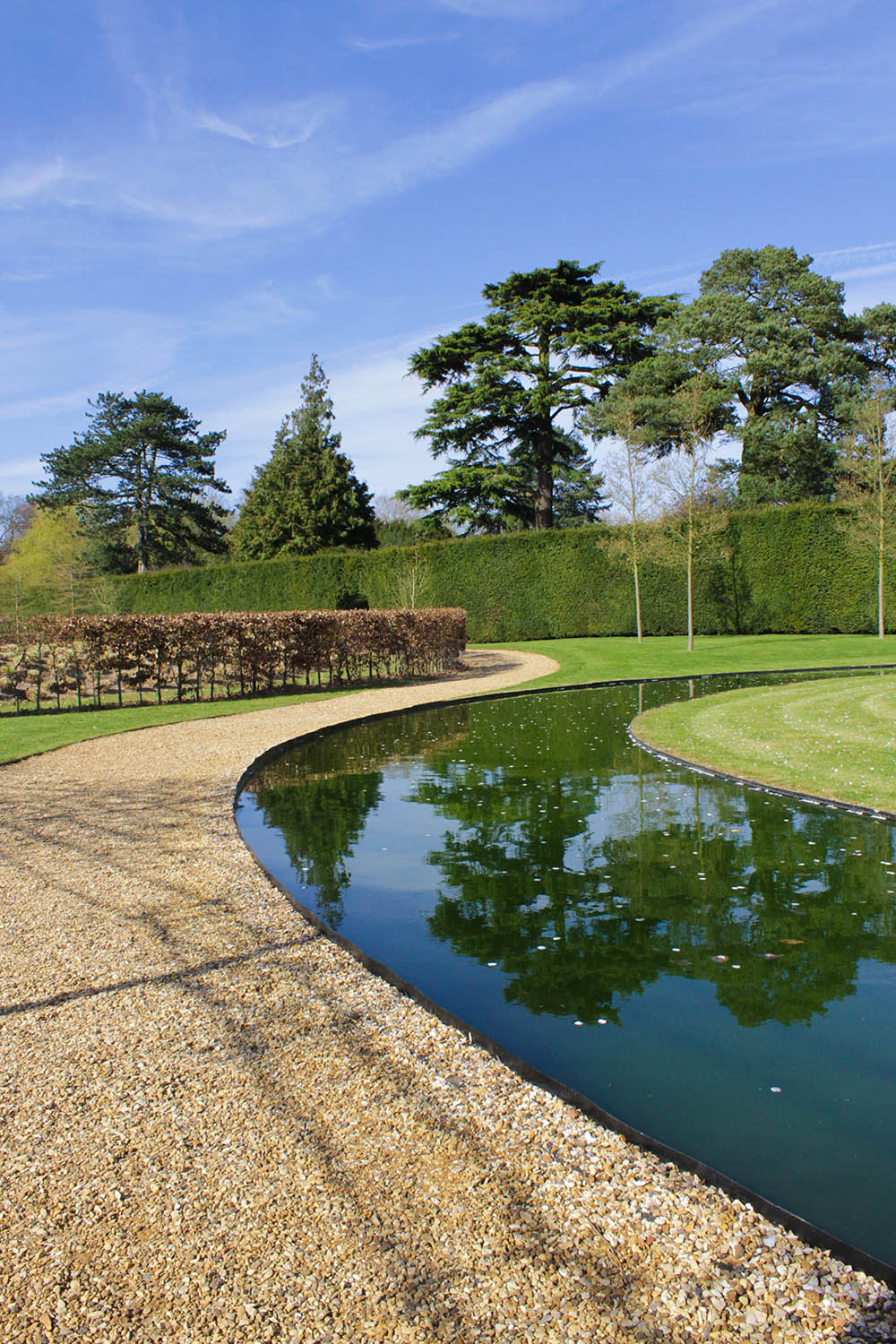 A landscaped garden with a path, water feature, grass and trees.