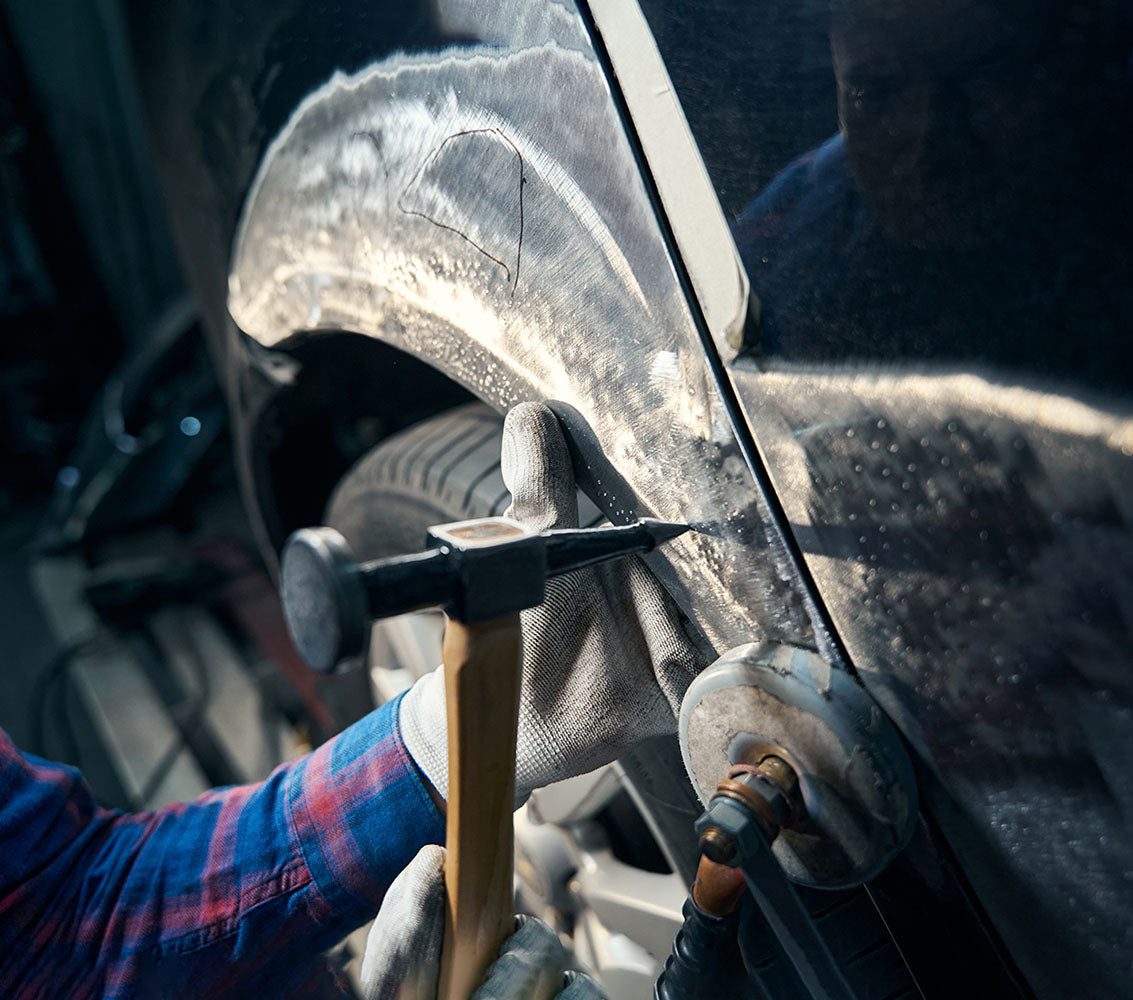 A skilled car body worker panel beating on the front wing of a classic car.
