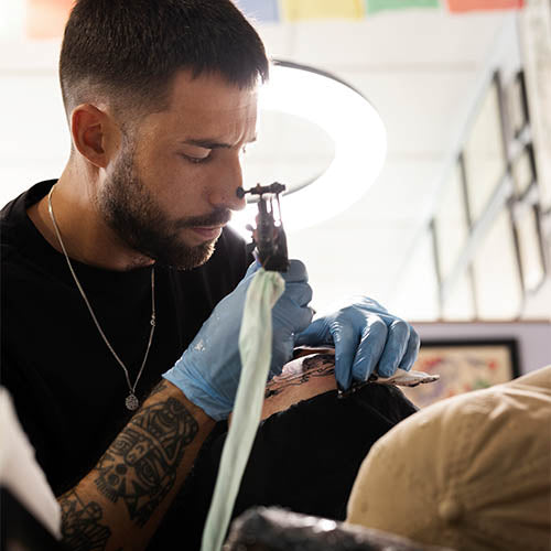 A tattoo artist tattooing a clients shoulder.