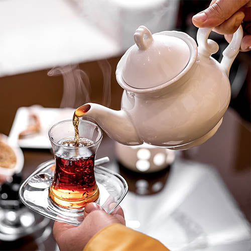 A tea room employee pouring tea from a teapot into a glass cup.