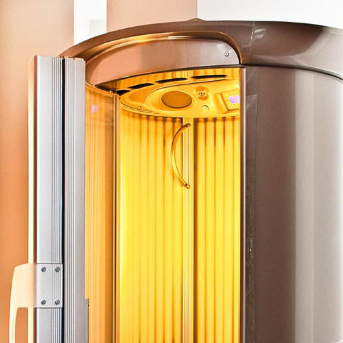 A vertical sunbed in a tanning salon with a warm orange glow.