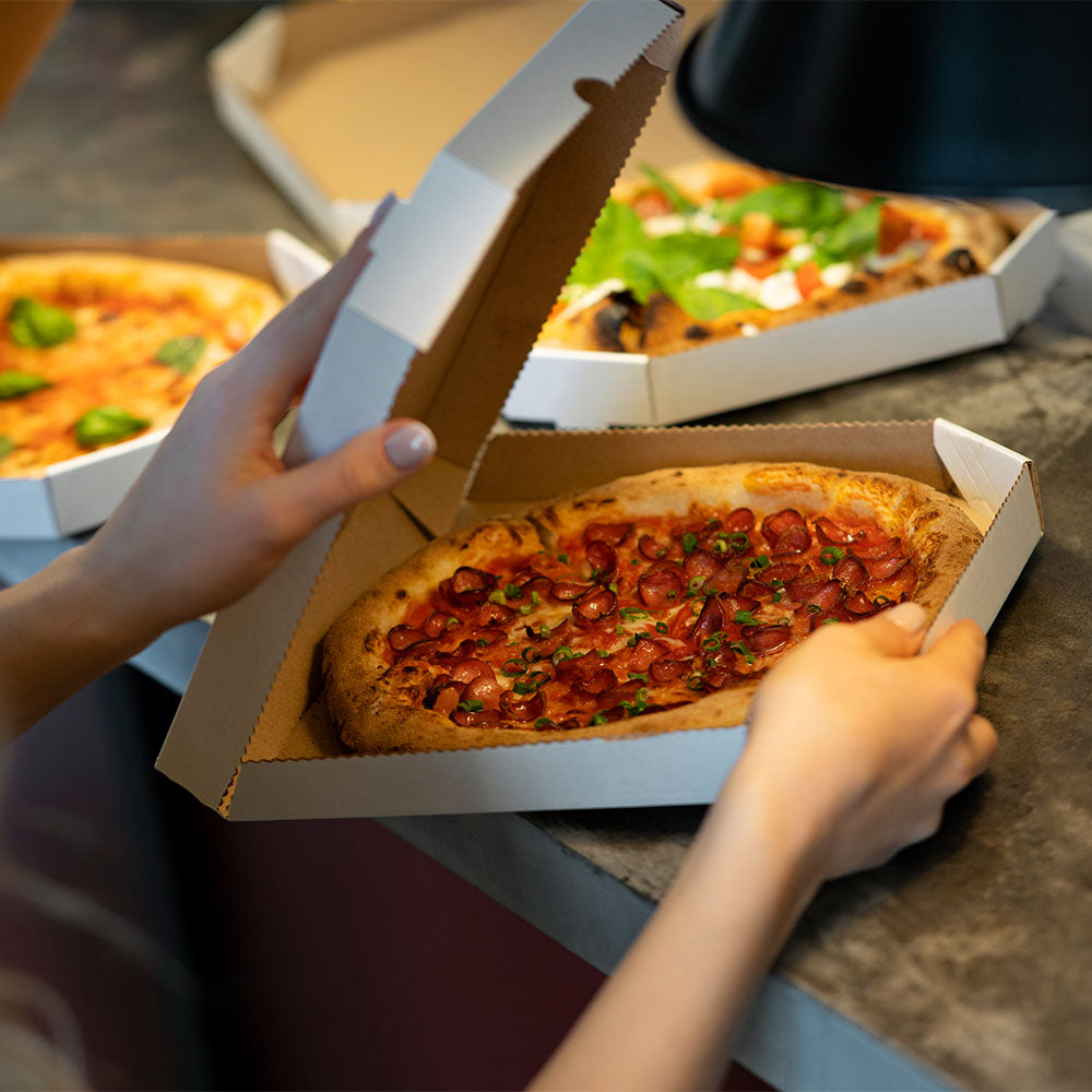 A woman holding a fresh takeaway pizza in a box.