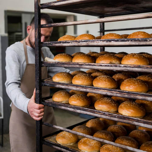 Bakery worker moves large bakery trolley full of fresh bread