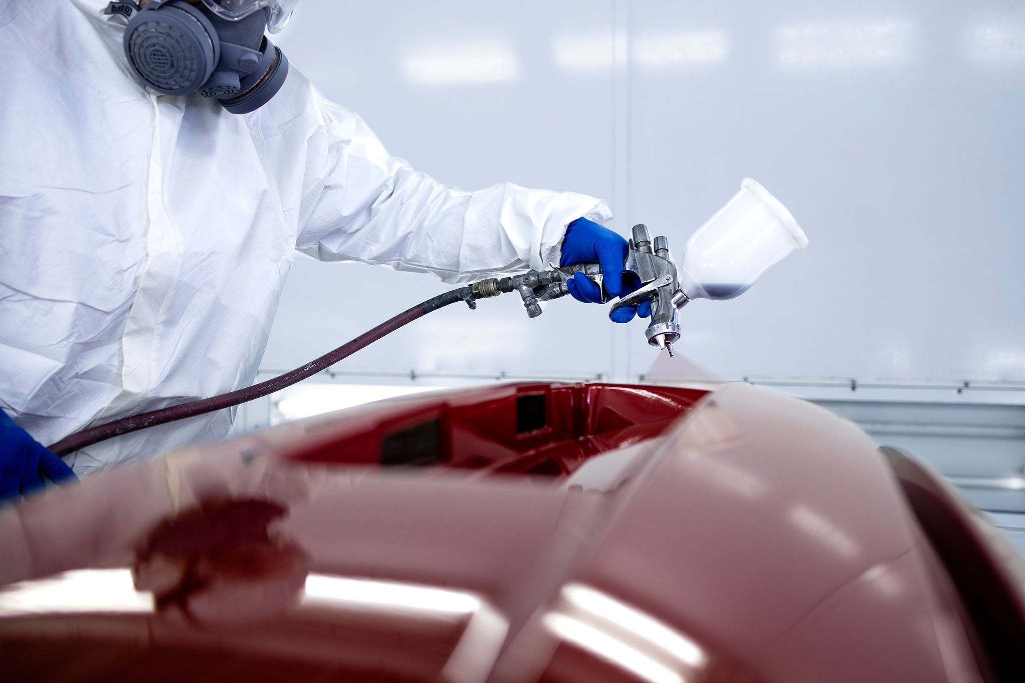 Car body shop employee painting car body panels with a paint spray gun.