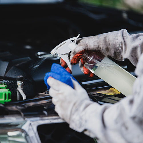 Car mechanic cleaning car parts with a spray bottle.