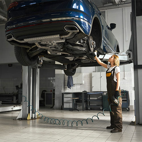Car mechanic working under a vehicle on a lift.