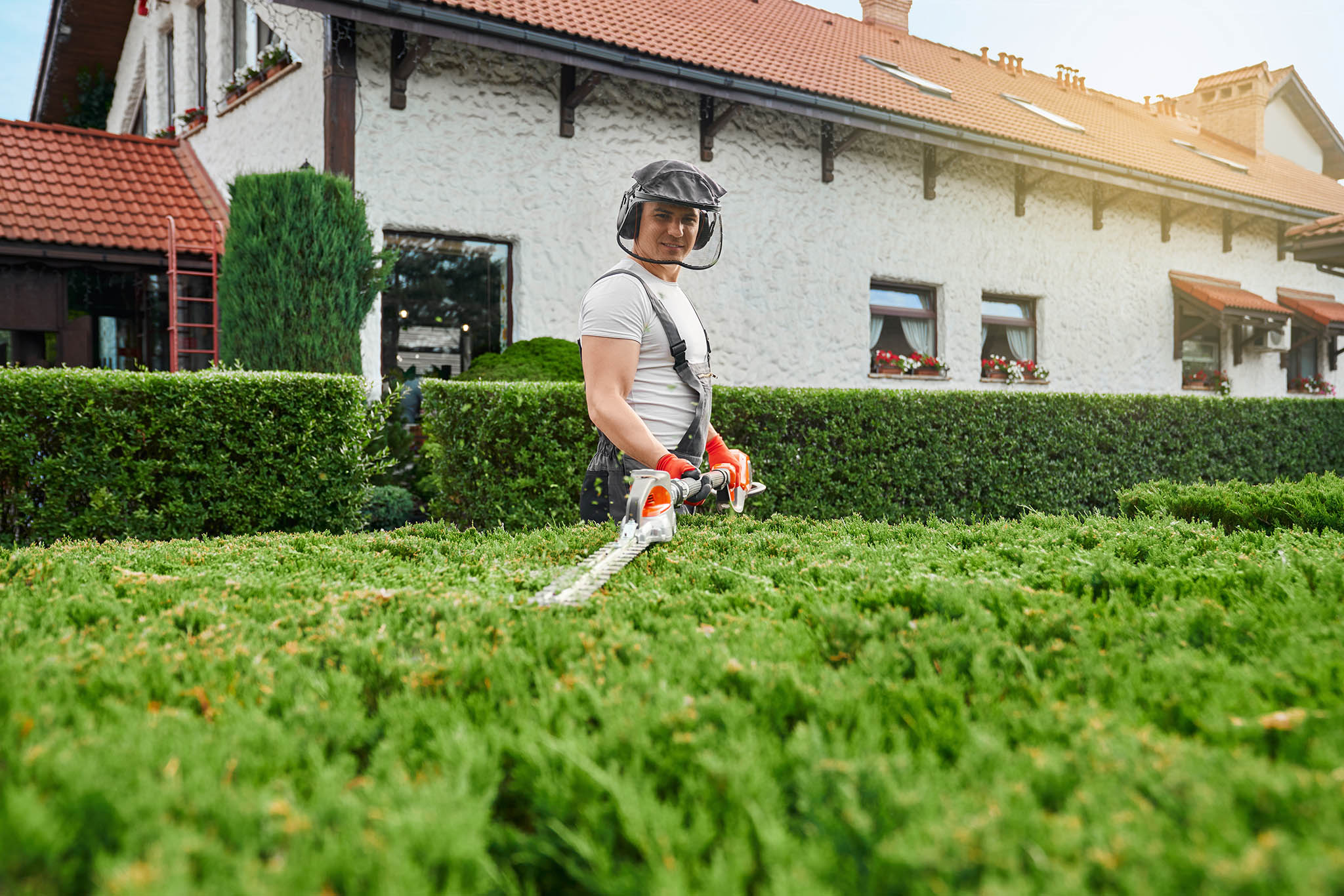 Gardener wearing safety glasses gloves pruning bushes in a customers garden.