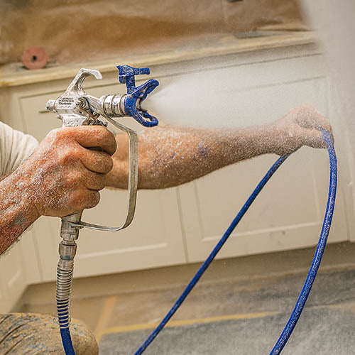 Hand holding airless spray gun to spray paint onto kitchen cupboard doors.