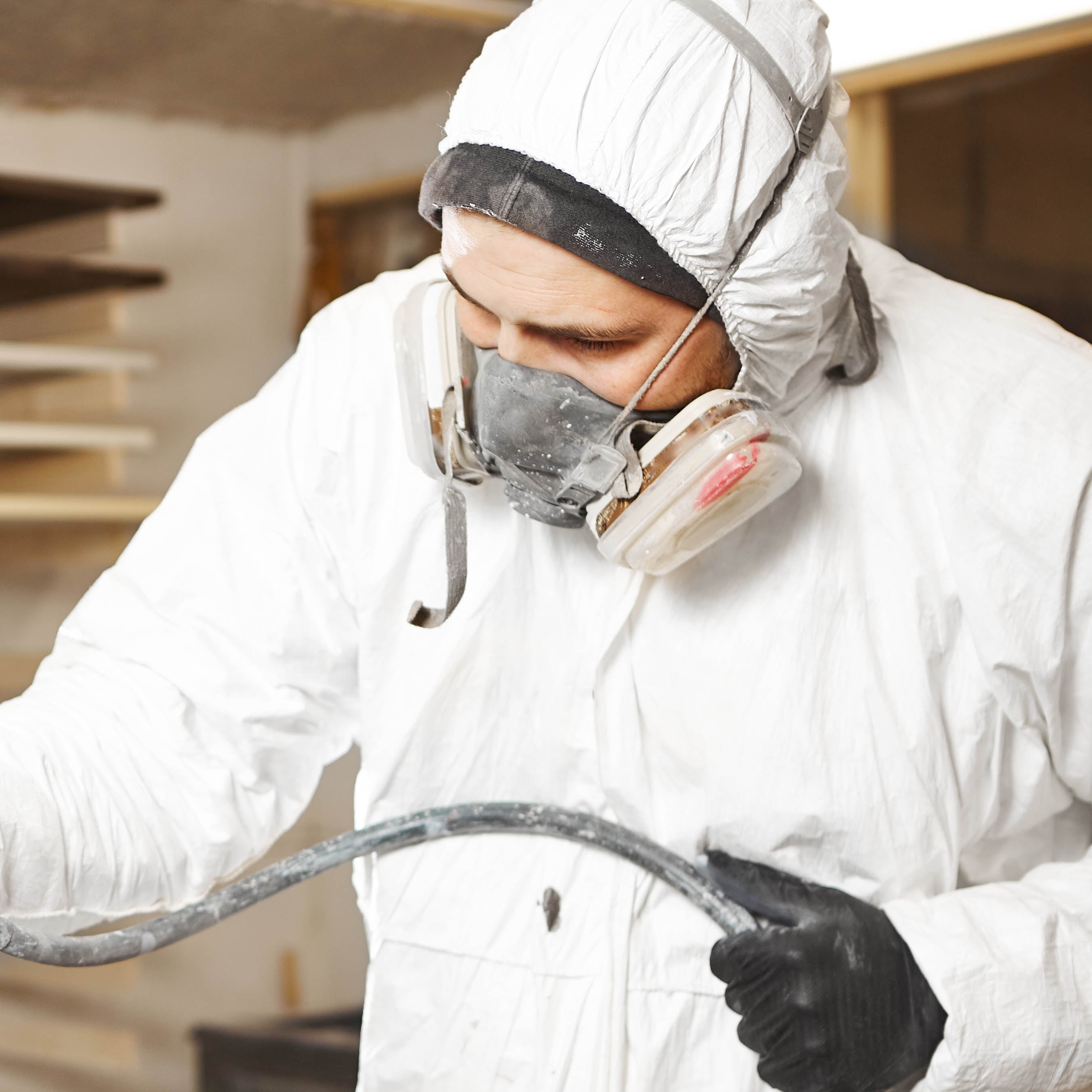 Kitchen spray painter wearing a half face dust mask while spraying paint onto kitchen cupboard doors.
