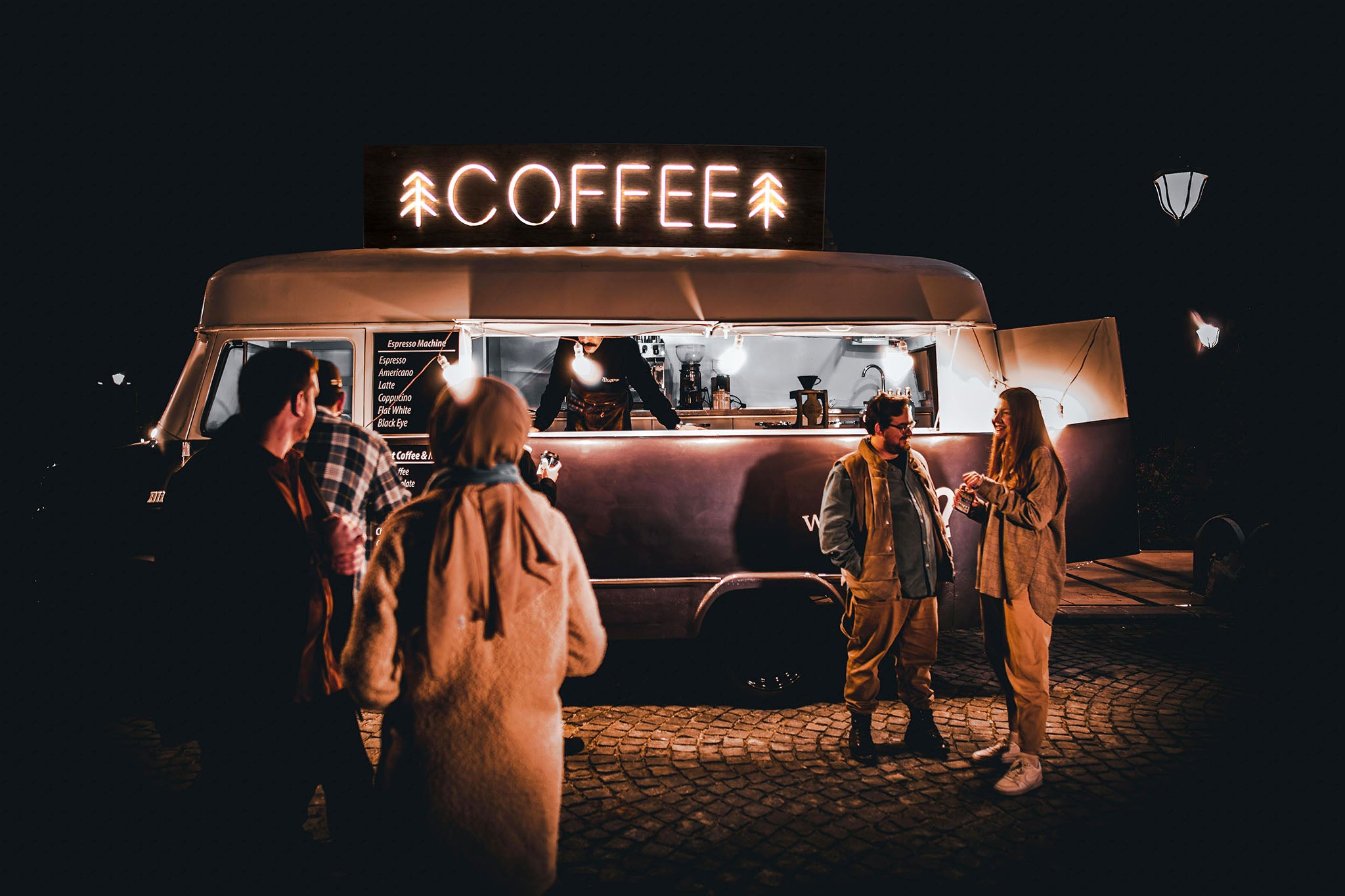 Mobile coffee shop owner serving customers at night.