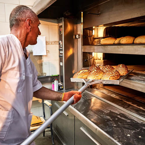 Professional baker removes freshly baked bread from an industrial oven in a bakery