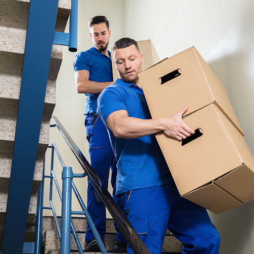Removal company workers carrying large boxes down some stairs.