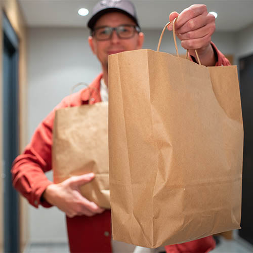 Takeaway food delivery worker holding paper bag full of food.