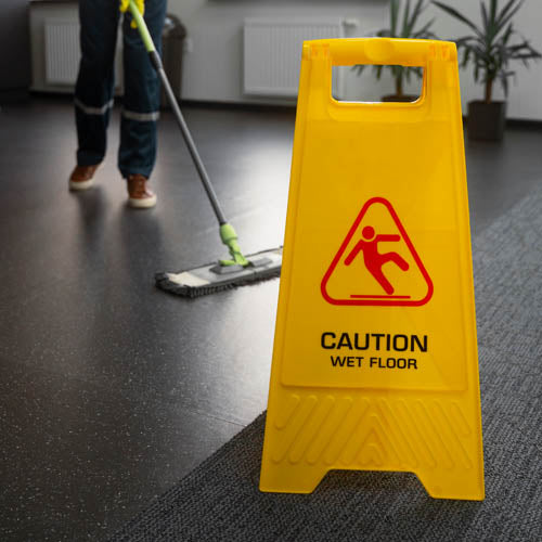 Wet floor sign with cleaning professional cleaning the floor in the background.
