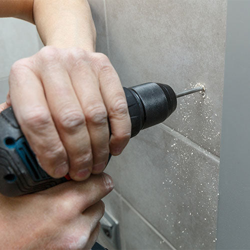 Bathroom fitter drilling into wall tiles for fixings during a bathroom installation, using power tools and safe drilling practices.