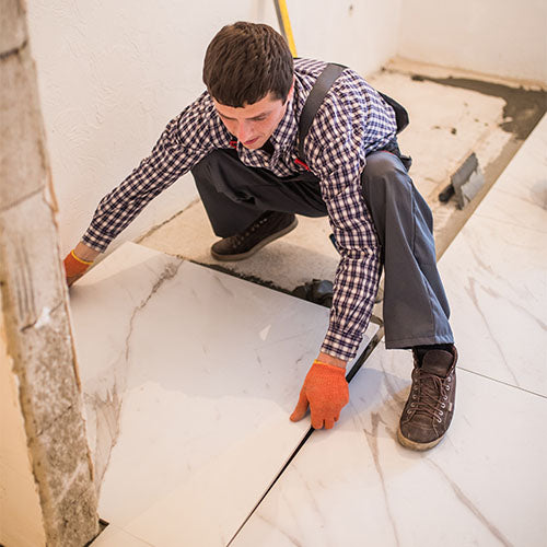 Bathroom fitter laying large floor tiles during a bathroom installation, fitting tile flooring as part of a bathroom refit.