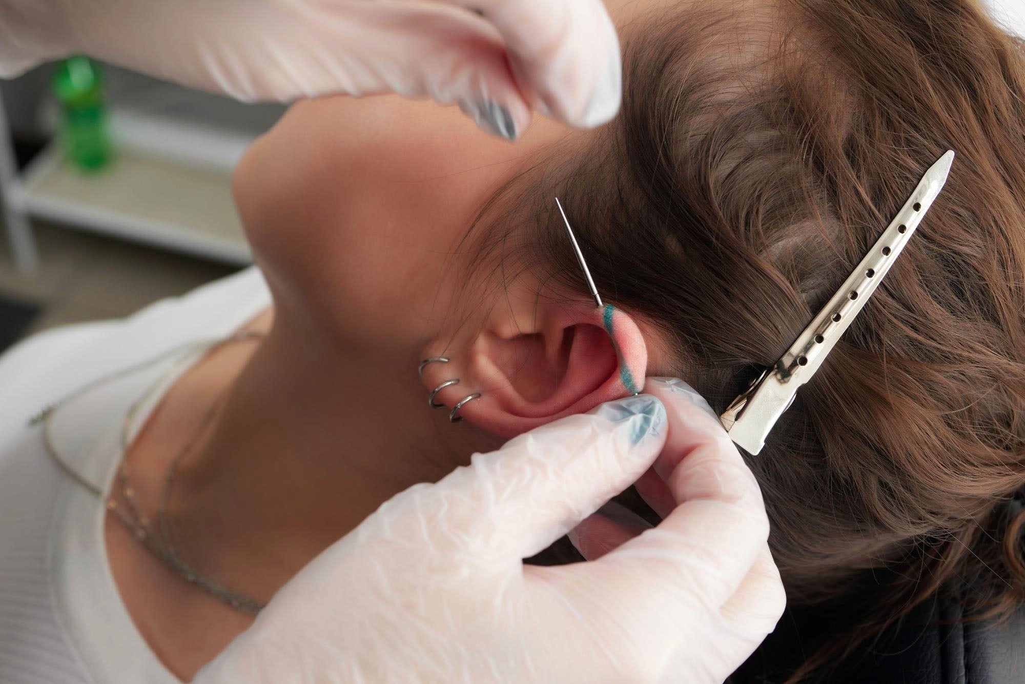 Body piercer carrying out an ear piercing procedure using gloves and a sterile needle in a body piercing studio.