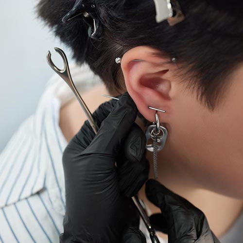 Body piercer carrying out an ear piercing procedure using sharps and gloves in a body piercing studio.