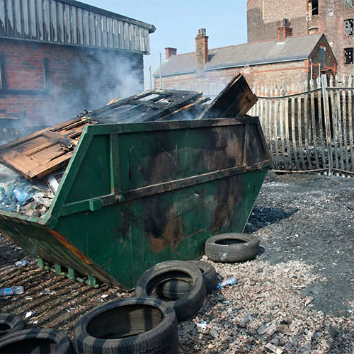 Burnt out skip in a yard after a waste fire, showing fire damage relevant to skip hire, waste transfer and waste disposal health and safety risks.