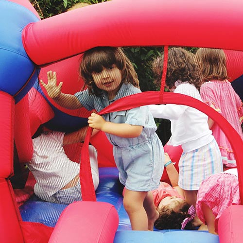 Children playing inside a colourful bouncy castle at an outdoor party, showing bouncy castle hire equipment in use.
