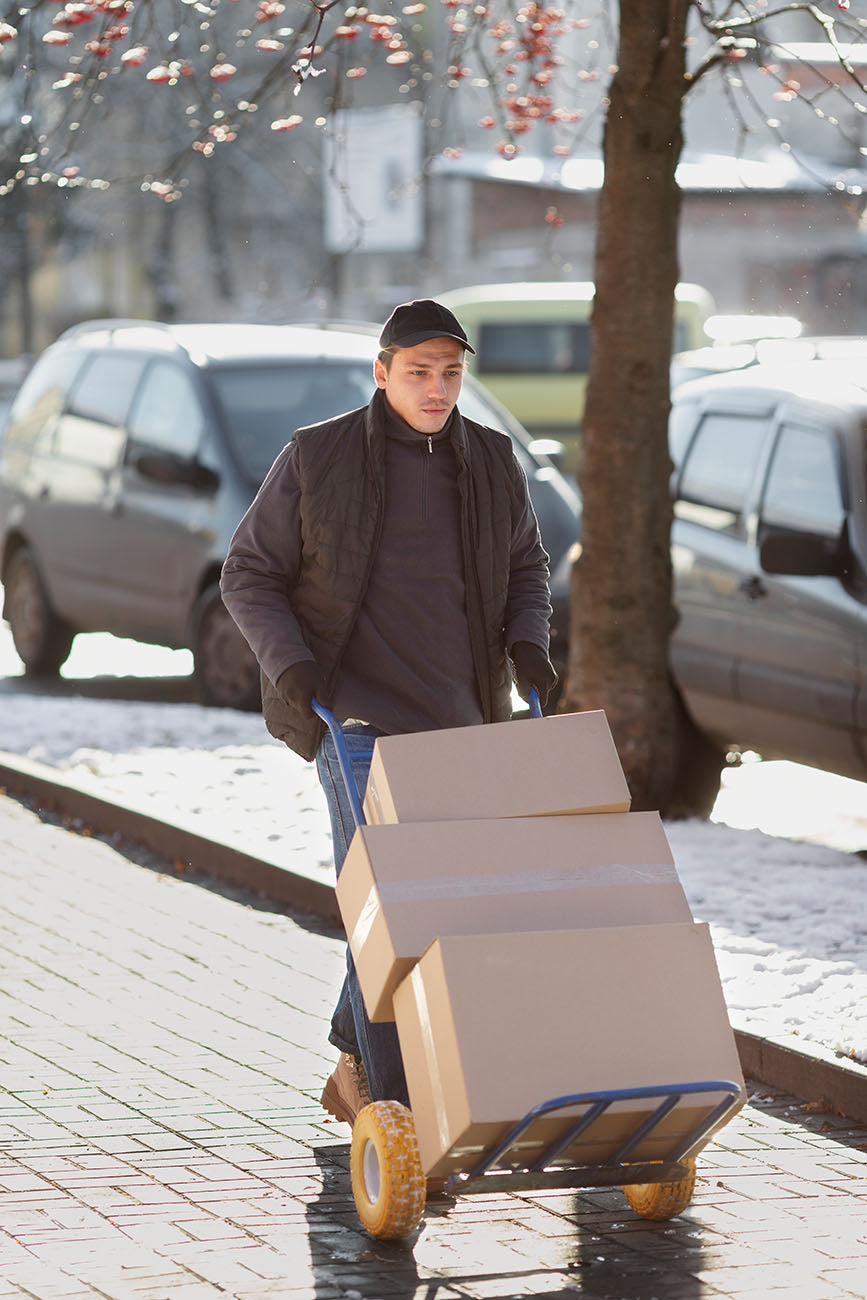 Courier moving parcels on a hand trolley along an icy pavement during a delivery.