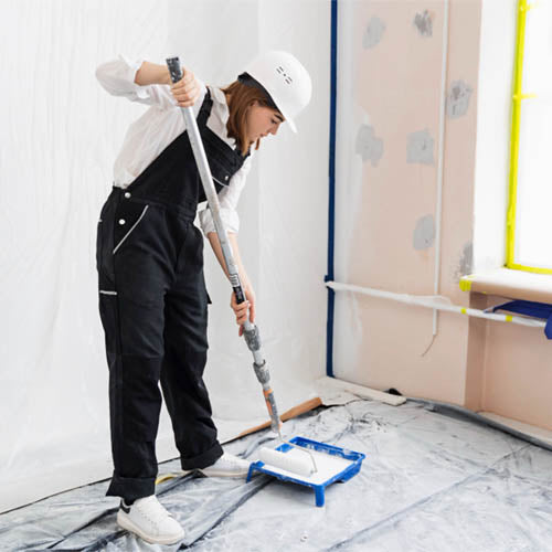 Female-decorator-leaning-over-to-add-paint-to-her-roller