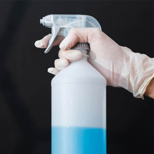 Hand wearing a glove holding a spray bottle with a dark background