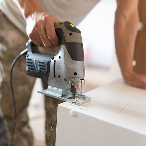 Kitchen fitter using a power tool to cut a kitchen cupboard during renovation work.