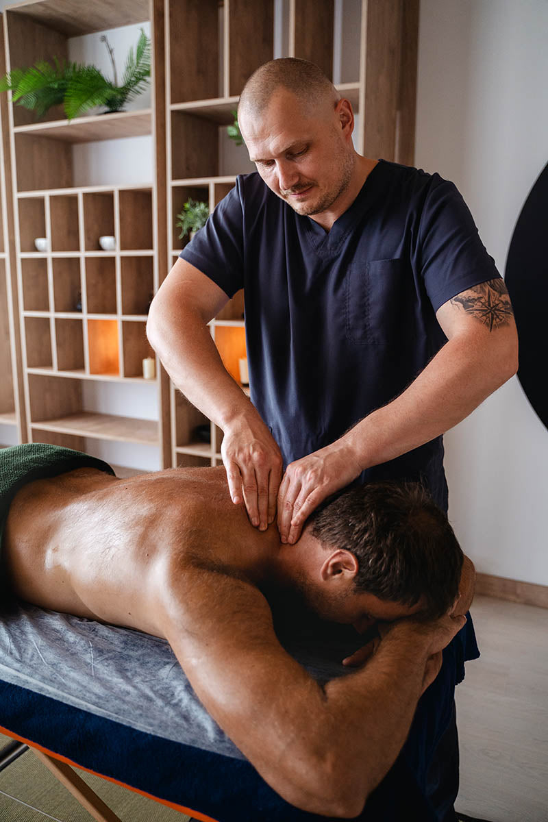 Massage therapist carrying out a neck and back massage treatment on a client in a professional treatment room.