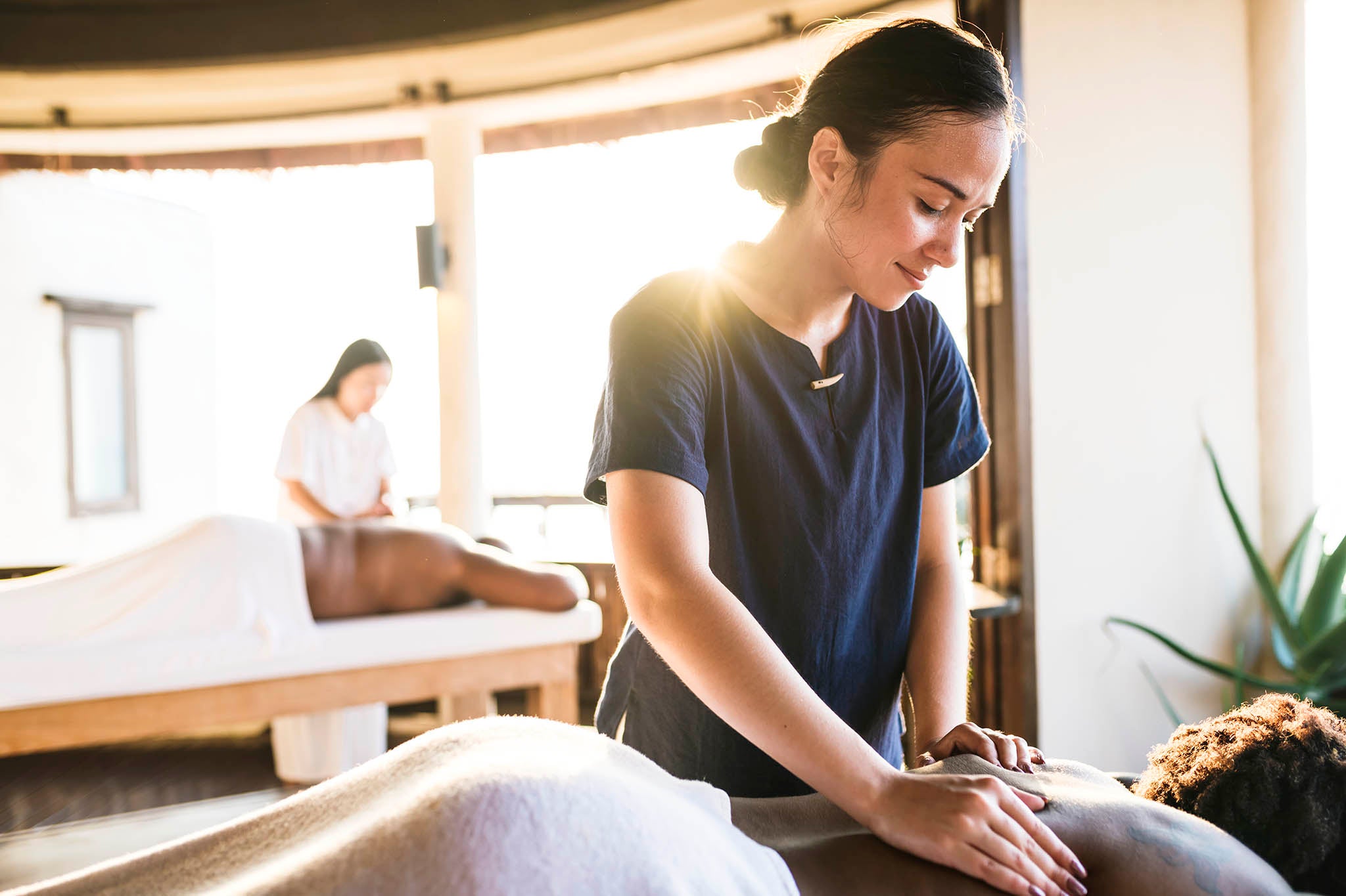 Massage therapist providing a professional massage treatment in a bright treatment room within a massage therapy clinic.