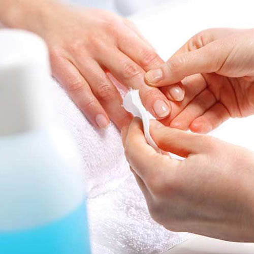 Nail technician using nail polish remover on a client's nails.