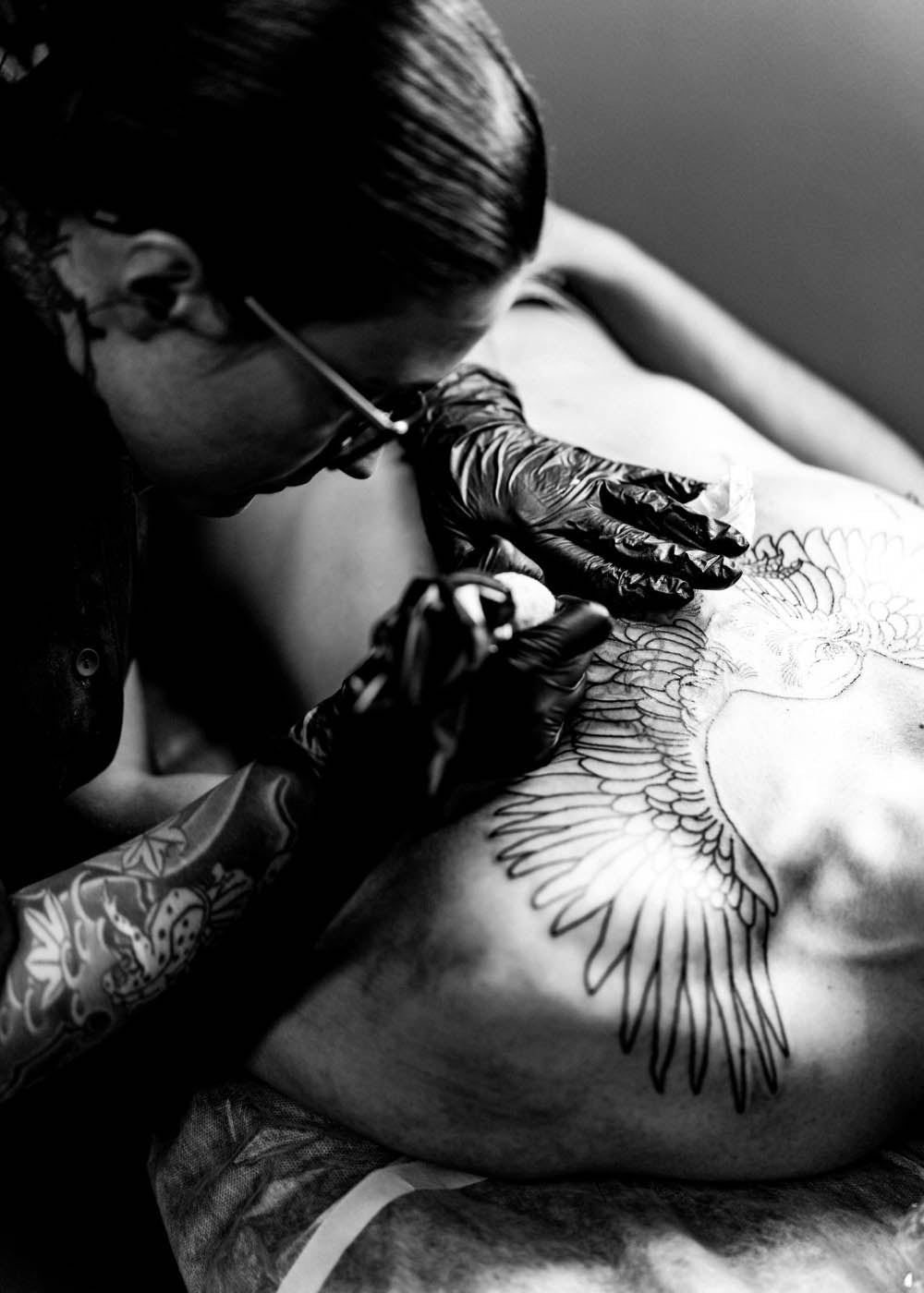 Tattooist tattooing a man's chest with a birds wing design