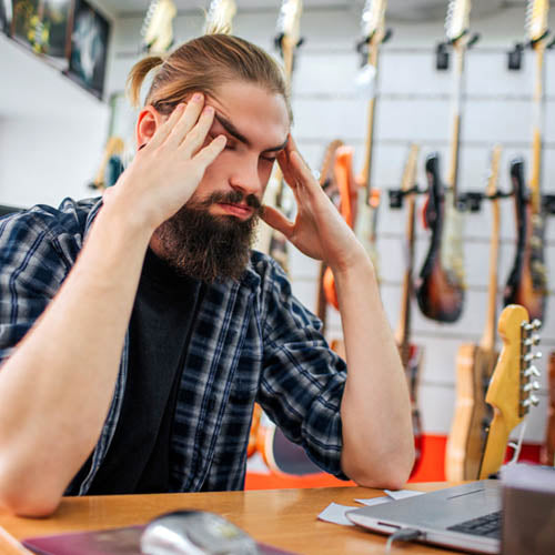 Young shop worker looking stressed with his head in his hands.